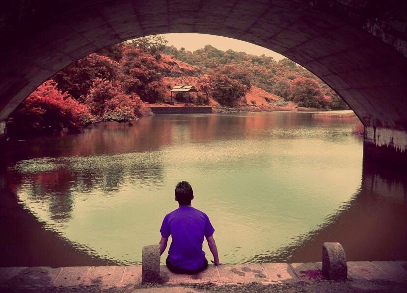 Person framed by a stone bridge arch beside a lake